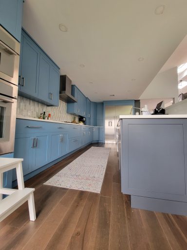 Modern kitchen with blue cabinets, white countertops, and wooden flooring.