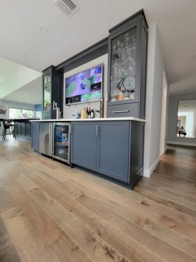 Modern kitchen with a blue island, a TV above, and light hardwood flooring.