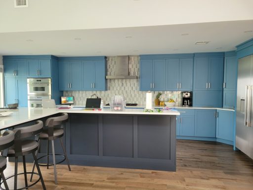 Modern kitchen with blue cabinets, light countertops, and hardwood flooring.