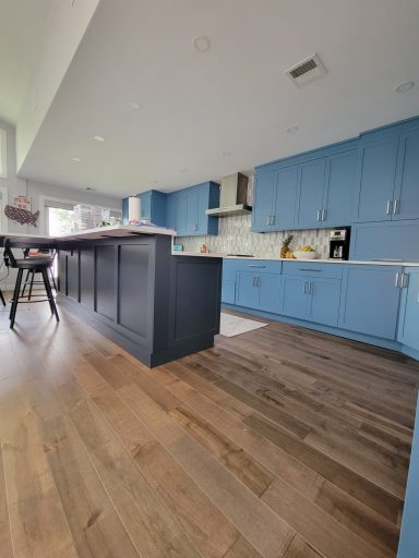 Modern kitchen with blue cabinets, white countertops, and wooden flooring.